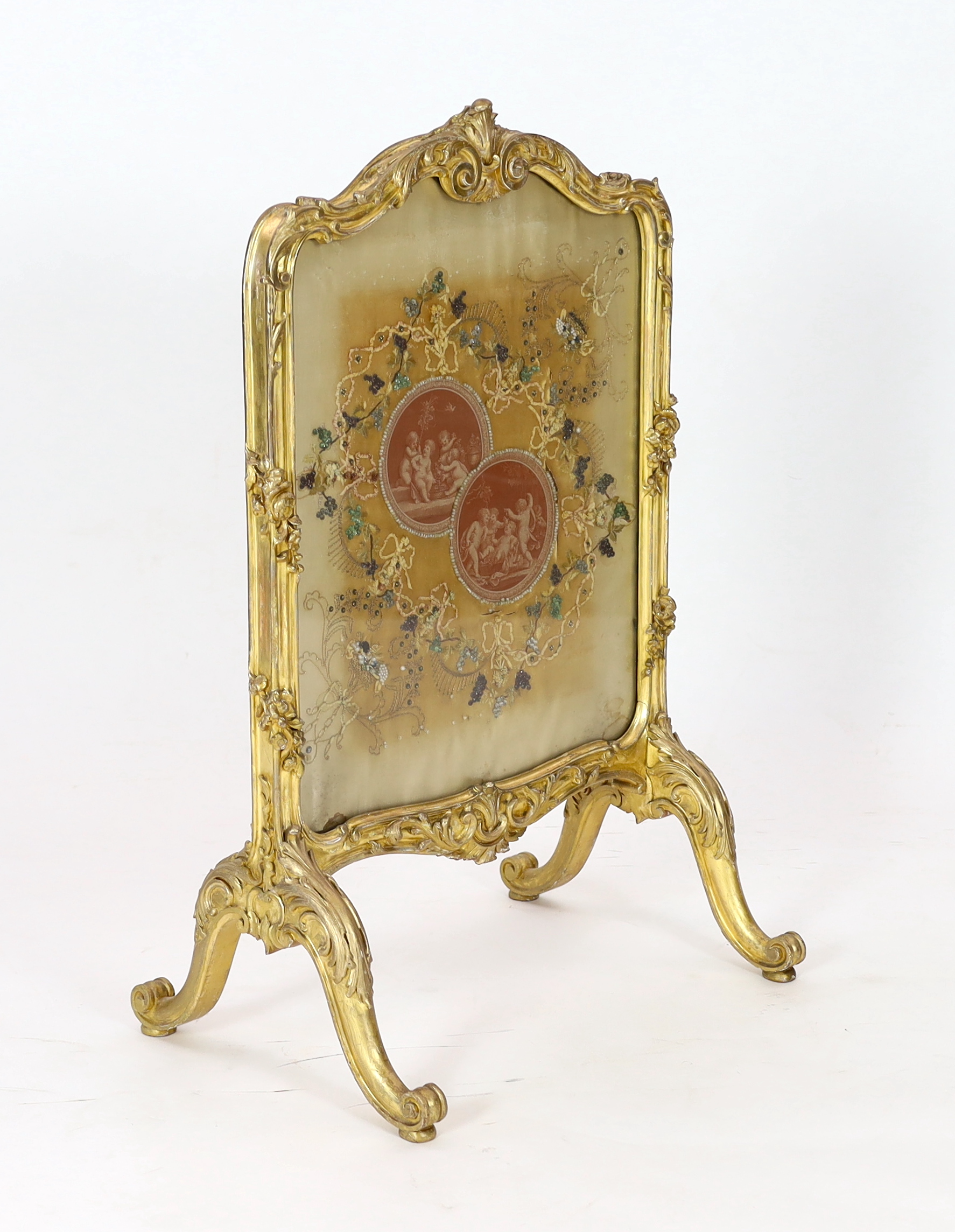 A Louis XV style carved giltwood framed fire screen, the silk panel printed with roundels of playful amorini, within naturalistic beadwork decorated foliage, 60cm wide, 93cm high. Condition - poor to fair, Please note th
